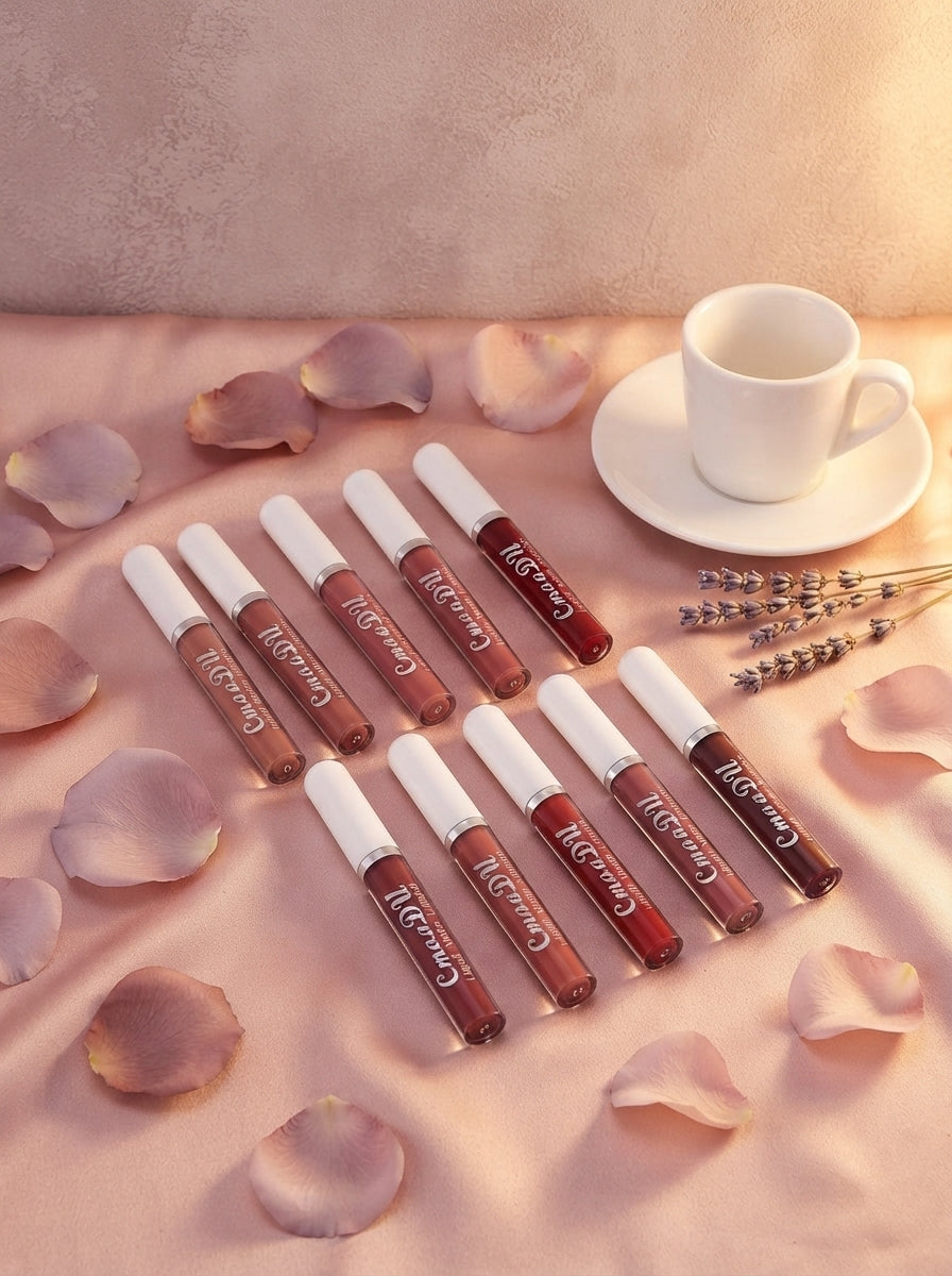 A set of ten matte lipstick tubes arranged on blush pink silk fabric with rose petals and a coffee cup on a warm surface.